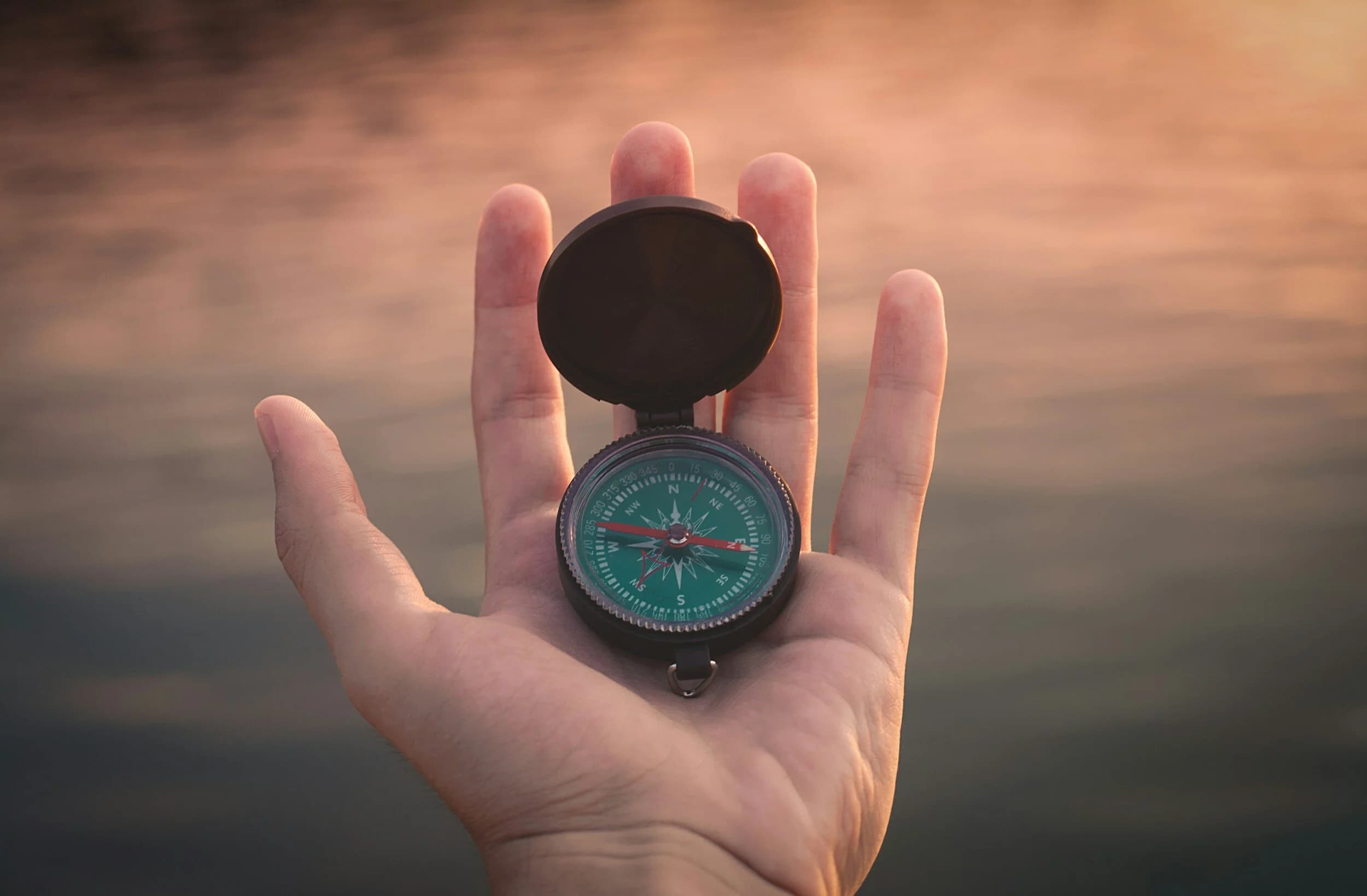 A hand holding a compass at sunset